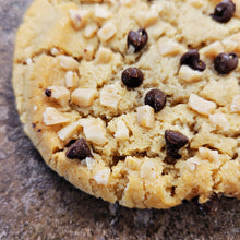 Load image into Gallery viewer, Close-up of a cookie with chocolate chips and tofffee bits on a textured surface