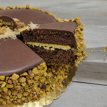 Load image into Gallery viewer, Chocolate cake with a slice cut out, showing layers on a wooden surface.