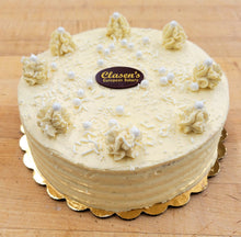 Load image into Gallery viewer, vanilla custard torte with buttercream frosting and white edible pearls on top, on a wooden surface.