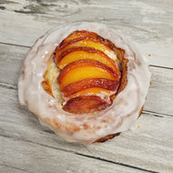 A Danish pastry with fresh peaches baked inside, on a wooden surface.