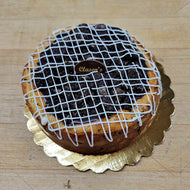 Cheesecake topped with crushed oreo cookies and white icing on a gold cake stand, branded 'Clasen's', on a wooden surface.