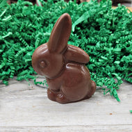 Chocolate rabbit on a wooden surface with green Easter grass in the background