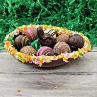 Chocolate nest with sprinkles filled with chocolate truffles and a chocolate bunny on a wooden surface with greenery in the background