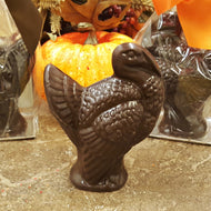 A dark chocolate turkey-shaped candy displayed in front of a pumpkin and decorative elements, indicating a seasonal or festive setting.